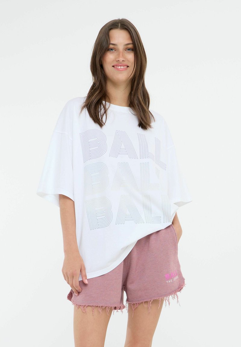 Hvit oversized t-skjorte med "BALL" trykt i grå linjer. Kombinert med rosa, slitte shorts med et logo i hvitt.