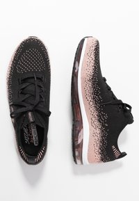 Svarta sportskor med graderade rosa accenter, överdel i mesh, snörningsdesign och genomskinlig luftkuddssula. Strukturerad mönster genom hela skon.