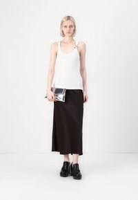 Bijela majica bez rukava s detaljem na ramenu, uparen s crnom satenskom midi suknjom. Izgled upotpunjuju robustne crne platforme i srebrna clutch torbica.