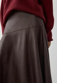 Primo piano di una gonna in pelle marrone scuro con cuciture diagonali, indossata con un maglione lavorato a maglia bordeaux.