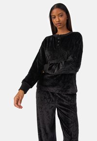 Conjunto de ropa de descanso de velour negro que incluye una camiseta de manga larga con tapeta de botones y pantalones sueltos. Ambos tienen un patrón abstracto texturizado.