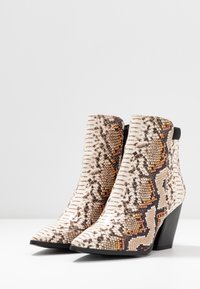 Botines cortos con un patrón de textura de serpiente en tonos beige, marrón y naranja. Punta afilada y tacón negro grueso.