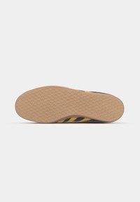 Black athletic shoe sole with honeycomb texture, featuring yellow and black stripes, rubber material, and rounded toe design.
