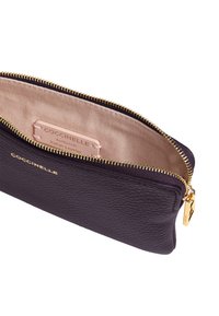 Pochette in pelle viola scuro con zip dorata. L'interno presenta una fodera in tessuto beige e un'etichetta del marchio ben visibile.