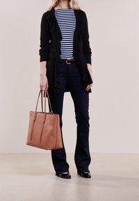 Svart volangcardigan över en marinblå och vit randig skjorta, tillsammans med mörka jeans och en tan läderhandväska. Svarta ballerinas på fötterna.