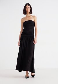 Abito maxi nero senza spalline con corpetto arricciato e gonna fluida. Realizzato in un tessuto liscio, presenta una parte superiore aderente e una parte inferiore morbida.