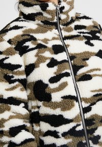 Fleecejacka med hög krage, kamouflagemönster i beige, svart och vitt, med framzipper och texturerad tyg.