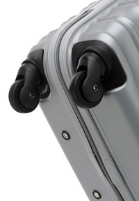 Silver hard-shell suitcase with textured surface, black wheels, and grey zipper detail, featuring a sleek, rounded design and reinforced corners.