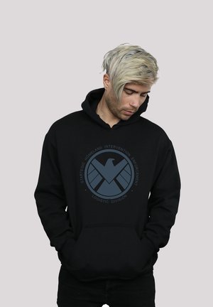 Black hoodie featuring a circular graphic with a stylized eagle logo and text. The fabric appears soft with a front pouch pocket and drawstring hood.