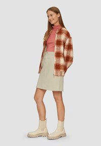 Rdzawy żakiet w deseń w kratkę z kremowymi akcentami, różowy golf, beżowa spódnica oraz kremowe botki na kostce z masywną podeszwą.