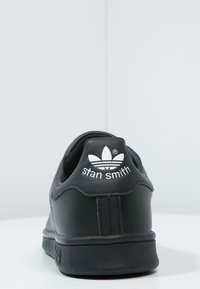 Svarta läder sneakers Stan Smith med en slät yta, med en vit logotyp och detaljer på hälen. Svart platt yttersula och minimalistisk design.