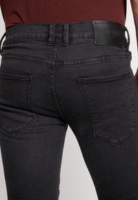 Černé džíny z denimu se slim fit střihem, pěti kapsami a koženou značkovou nášivkou. Materiál má hladkou texturu s jemnými detaily v prošívání.