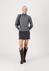 Siv turtleneck pulover, črna denimska krila s studenčki, rjave škornje do kolen z embosiranim vzorcem in mala črna torbica.