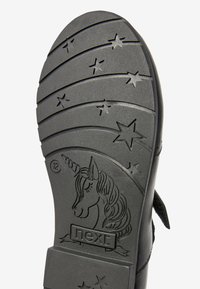 Schwarze Gummisohle mit einem Einhorn-Design und Sternmustern, mit erhöhten Linien für besseren Halt. Markenname "next" eingraviert.