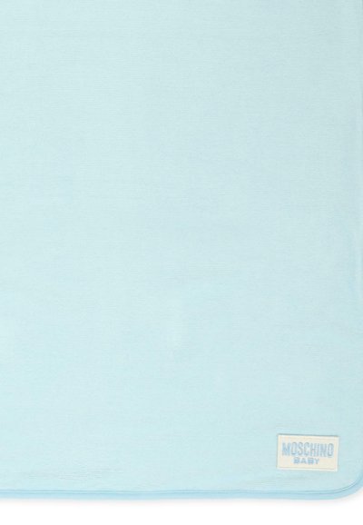 Jasnoniebieski kocyk dla niemowląt o miękkiej teksturze. Posiada stębnowane wykończenie oraz białą metkę z napisem "MOSCHINO BABY" w jasnoniebieskiej czcionce.