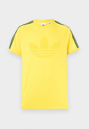 Žuta majica s teksturiranim printom logotipa u sredini. Ima zelene bočne pruge na raglan rukavima. Izrađena od glatkog pamučnog materijala.