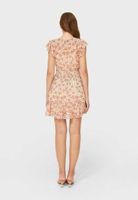 Vestido floral con mangas cortas con volantes, en colores rosa claro y crema, con un corpiño fruncido y un dobladillo de volantes en capas, visto desde la parte trasera.