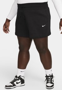 Fekete sportos rövidnadrág, kötőszalaggal a derékrészen, bal lábszáron fehér Nike logóval. Fekete-fehér magasszárú edzőcipőkkel párosítva.