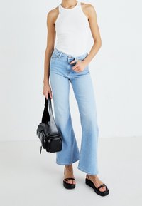 Ljust blå utsvängda jeans med hög midja, i kombination med en vit ärmlös topp och svarta platåsandaler. Svart crossbody-väska med fickor.