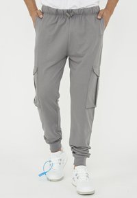 Grå sweatsbyxor med elastisk midja, sidofickor och cargofickor. Tillverkade av mjukt tyg, smalnande manschetter, kombinerat med vita sneakers.