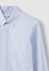 Svijetlo plava uska košulja na kopčanje s prednjim džepom i ovratnikom s gumbima, prikazana na jednostavnoj pozadini.