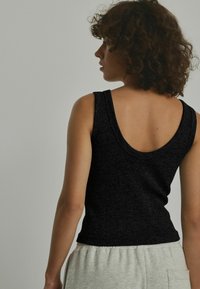 Canottiera nera con texture a costine, caratterizzata da uno scollo ampio sulla schiena e design aderente, abbinata a pantaloni della tuta grigi chiari.