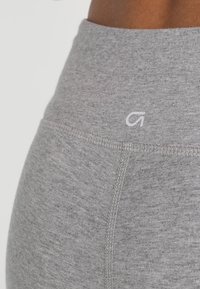 Leggings grigi alti in vita realizzati in tessuto morbido, con una texture liscia e un dettaglio con logo bianco vicino all'elastico in vita.