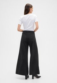 Calças pretas de perna larga feitas de ganga, com cintura alta, dois bolsos traseiros e textura suave, combinadas com um top branco de mangas curtas.