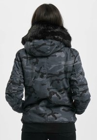 Sort og grå camouflageparka med pelsforet hætte, featuring en frontlynlås, lommer på ærmerne og ribbede manchetter. Tekstureret stof.