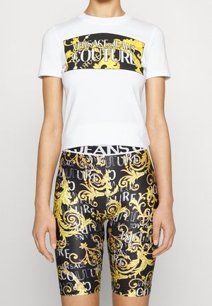 Camisa blanca de manga corta con estampado gráfico en negro y dorado, combinada con pantalones cortos negros que presentan un diseño y texto ornamentados en dorado y blanco.