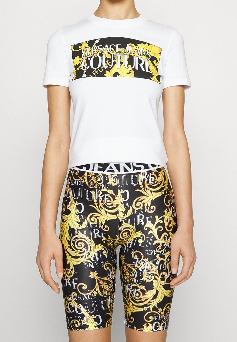 Vit kortärmad skjorta med svart och guld grafiskt tryck, tillsammans med svarta shorts med ett guld- och vitt utsmyckat mönster och text.