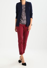 Blazer navy, top grigio floreale, pantaloni bordeaux e ballerine nere a punta. L'outfit presenta linee sartoriali e una combinazione di texture.