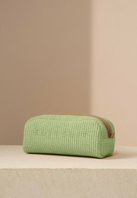 Groene, geweven toilettas met een rechthoekige vorm, gegraveerde merknaam en een ritssluiting met een tan accent. Gelaagd oppervlak.
