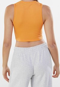 Top corto attillato in materiale a coste arancione con scollatura alta, abbinato a pantaloni sportivi grigi con vita elastica.