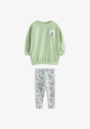 Jasnozielona bluzka z długim rękawem z naszywką księżniczki w połączeniu z białymi legginsami ozdobionymi wielokolorowym wzorem kwiatów i liści.