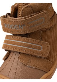 Zapato marrón para niños con parte superior de gamuza y malla. Cuenta con tiras de Velcro con acentos grises y una suela de goma texturizada.