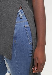 Top de punto gris con aberturas laterales, combinado con jeans de mezclilla ajustados de color azul que presentan un patrón desgastado en las rodillas.