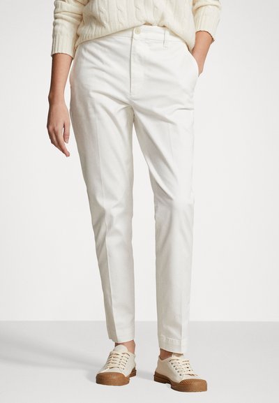 Pantalon en coton blanc avec une coupe ajustée, comportant des poches latérales, une fermeture à bouton et des ourlets à revers. Associé à des baskets de couleur claire.