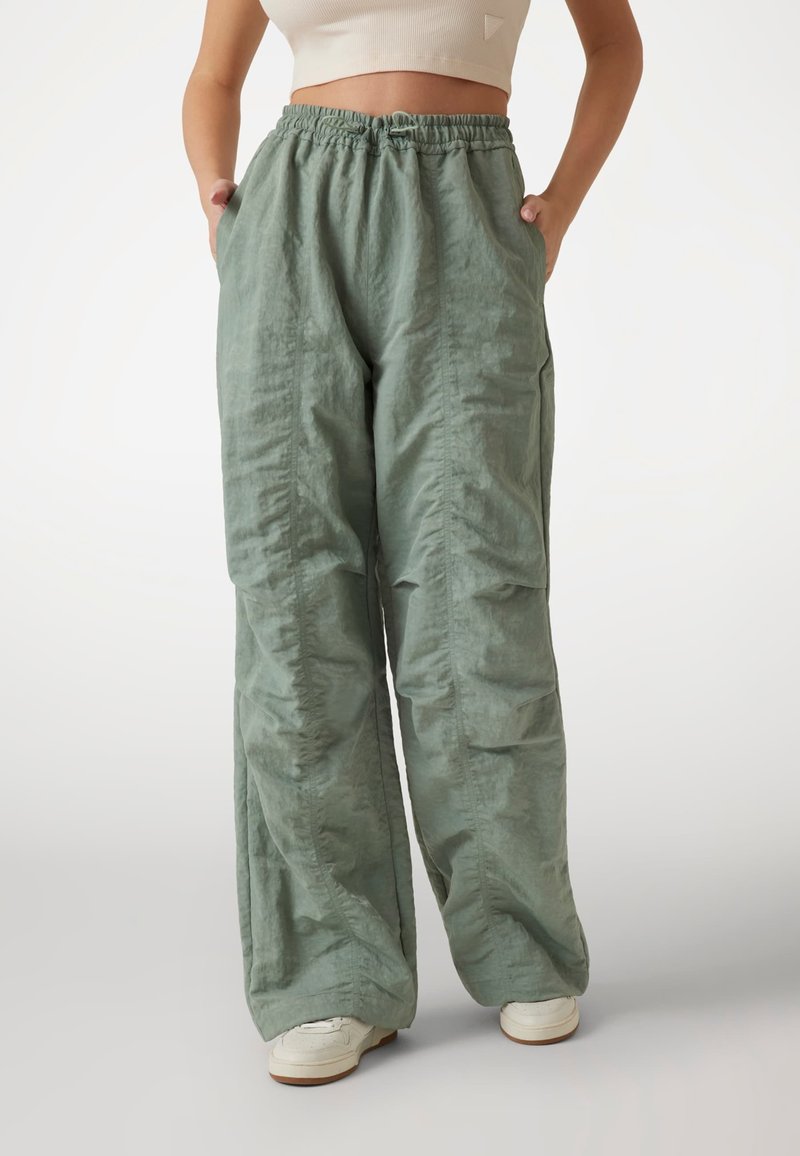 Pantaloni larga de culoare verde deschis, confecționați dintr-un material texturat. Au un elastic în talie și buzunare laterale. Fără modele sau accesorii vizibile.