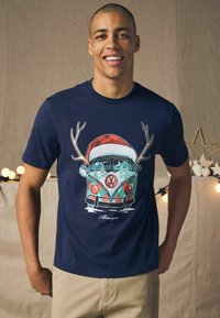 Mørkeblå bomulds t-shirt med et grafisk motiv af en Volkswagen-varevogn med gevirer, en juleslæde og vintertræer; kortærmet og med rund halsdesign.