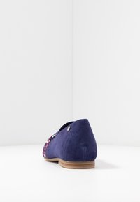 Ballerines en daim bleu marine avec un petit talon, dotées d'une accent floral à l'avant et d'un détail métallique circulaire près du talon.