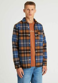 Geruite shirt in blauw, bruin en crème, met een knoopsluiting en een borstzak. Draag het over een bruine t-shirt en combineer het met een spijkerbroek.