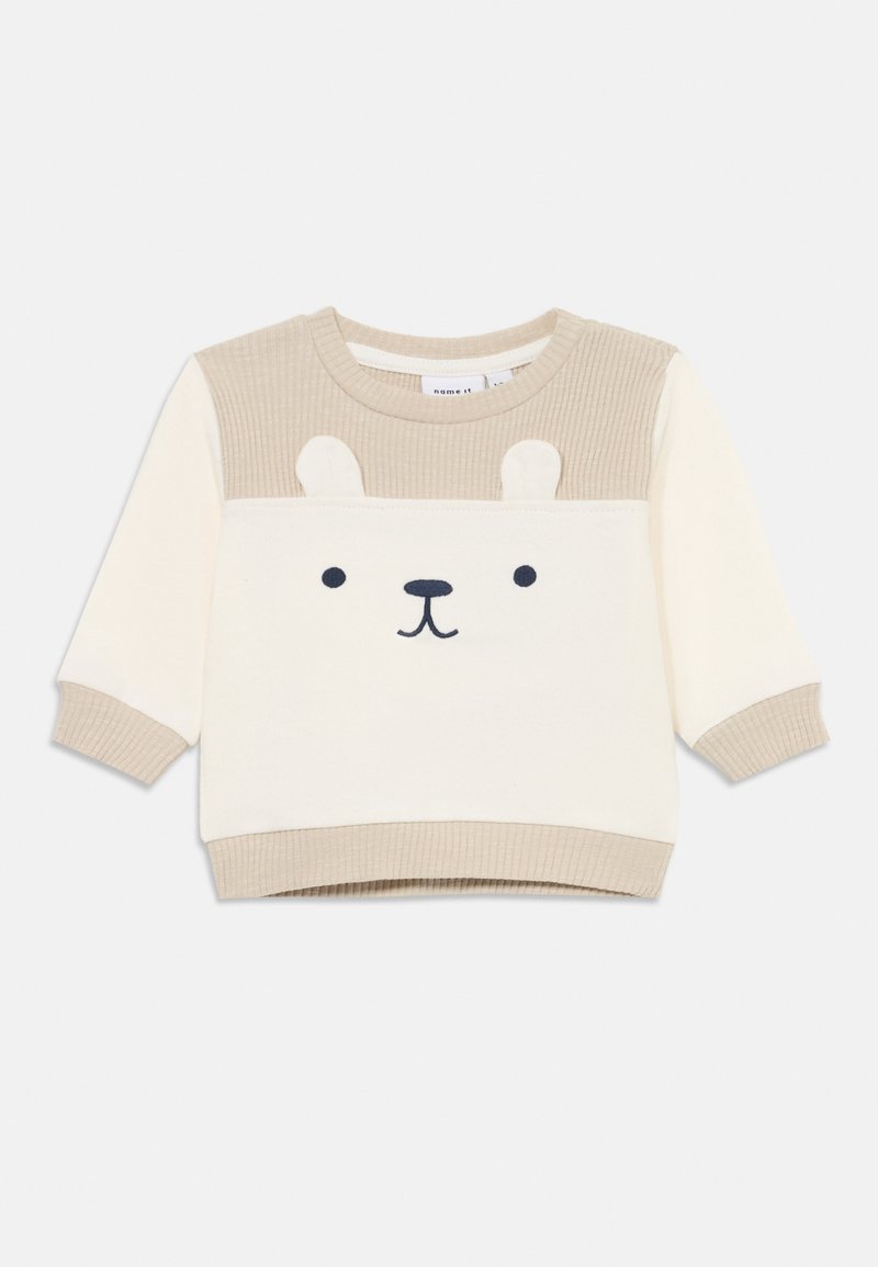 Beige og kremfarget genser med stripete tekstur. Har et bjørneansiktsdesign, rund hals og ribbestrikkede lange ermer.