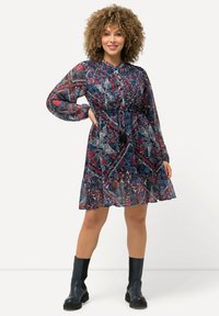 Chiffon-mekko, jossa on sininen ja punainen kukkakuosi, pitkät hihat ja joustava vyötärö. Yhdistetty mustiin nilkkabootseihin kontrastia varten.