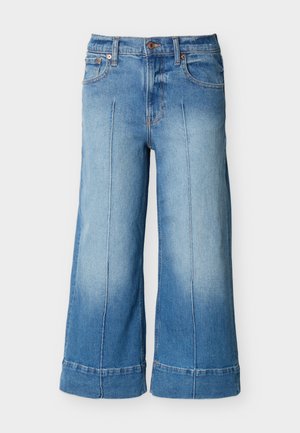 Jean large de couleur bleu clair, coupé court, avec poches avant, passants pour ceinture, fermeture par bouton et détails de coutures verticales le long des jambes.