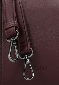Bordeauxrote Ledertasche mit strukturiertem Finish, doppelten Metallverschlüssen und embossed Logo. Die Riemen weisen feine Nähte auf.