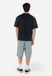 Černé tričko s krátkým rukávem, bavlněný materiál, pohodlný střih; spárované se světlými modrými džíny, casual styl. Černobráná obuv.