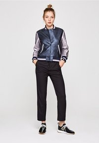 Giacca bomber in pelle blu navy con maniche argentate, abbinata a pantaloni neri a righe e sneakers nere. Tessuto strutturato in tutto.