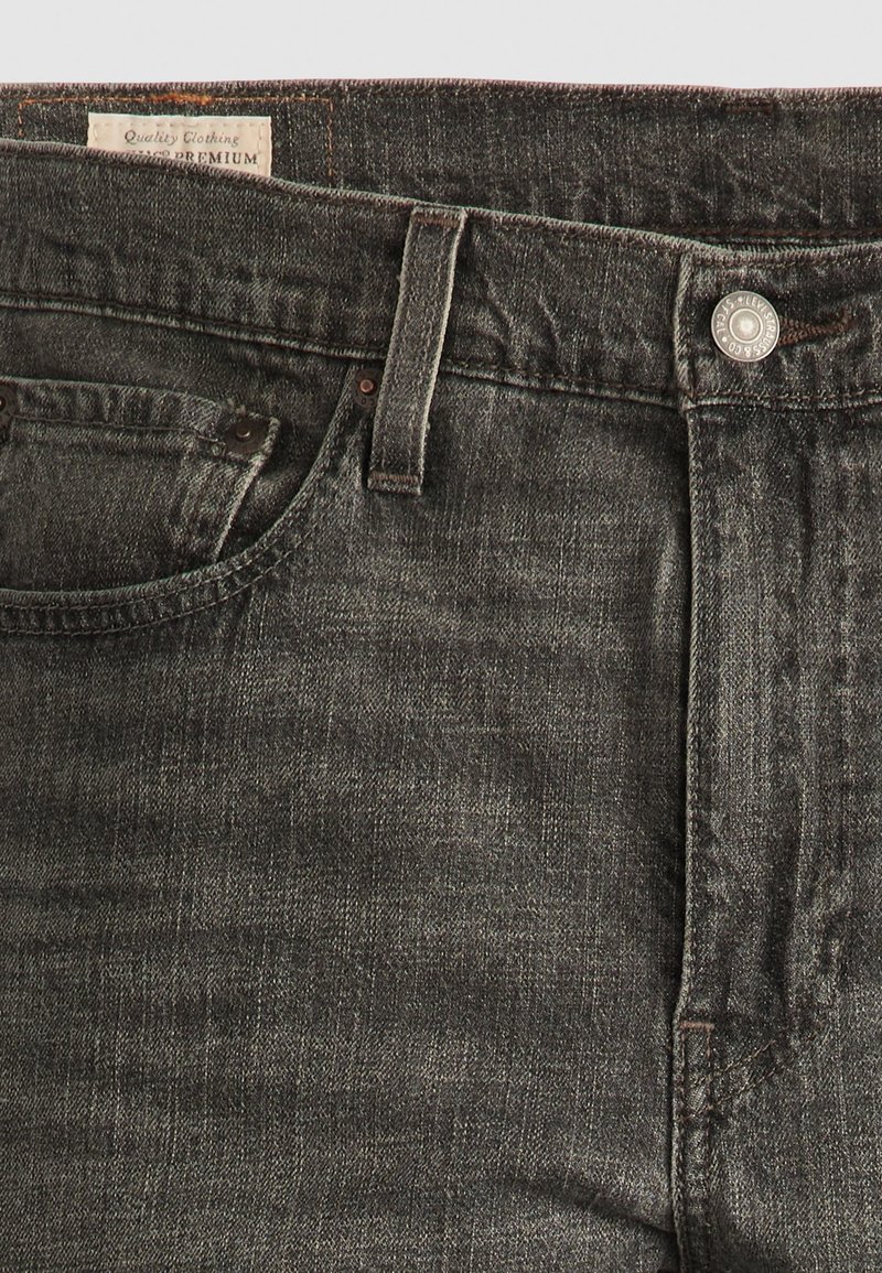 Jean en denim gris foncé avec une finition texturée, comprenant une poche avant, un bouton en métal et des détails de couture le long de la taille.
