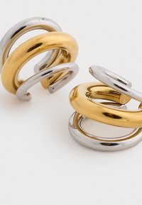 Arany és ezüst spirális karika fülbevalók sima, fényes felülettel és váltakozó színekkel, három összefonódott gyűrűt bemutató merész kialakítással.